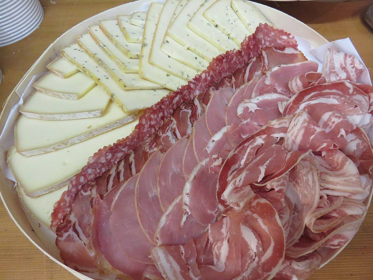Un plateau de tranches de fromage à raclette, dont certaines au poivre, et de charcuterie