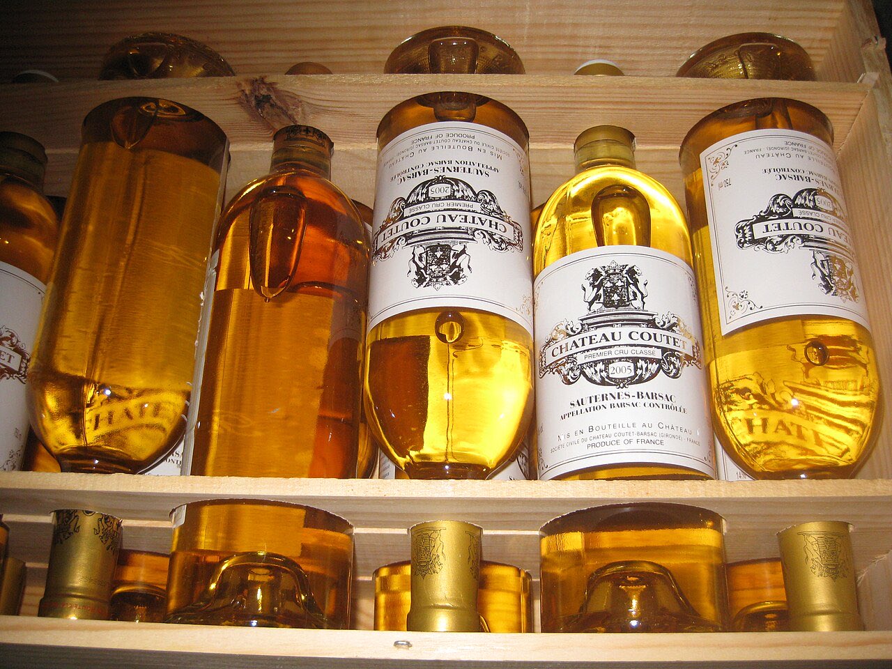 Des bouteilles de Château Coutet 2005 à la robe dorée, couchées dans une caisse en bois