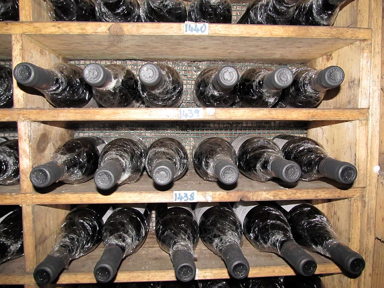 Des bouteilles couvertes de poussière, couchées sur des étagères en bois