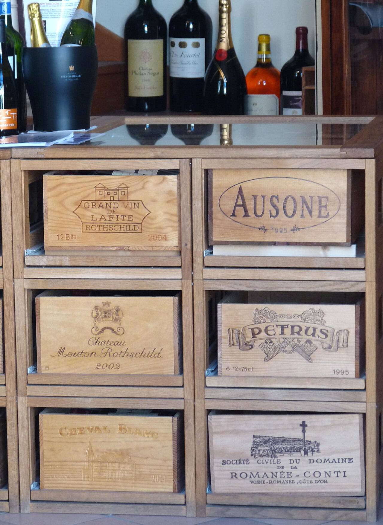Un meuble de présentation garni de six façades de caisses en bois de Lafite Rothschild, Mouton Rothschild, Cheval Blanc, Ausone, Petrus et Romanée-Conti, sous des bouteilles