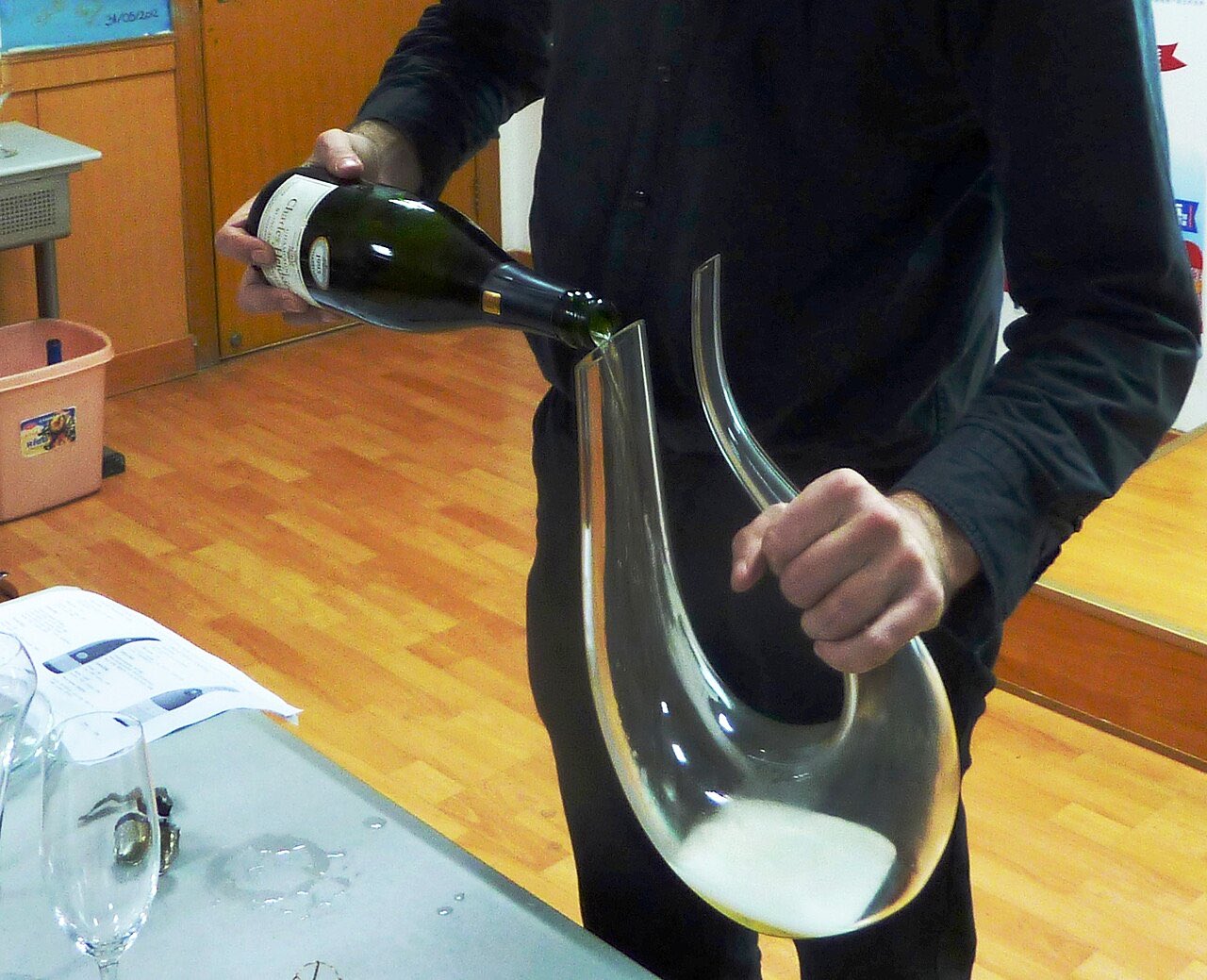 Un homme verse une bouteille de champagne dans une carafe en verre, lors d’un atelier de dégustation