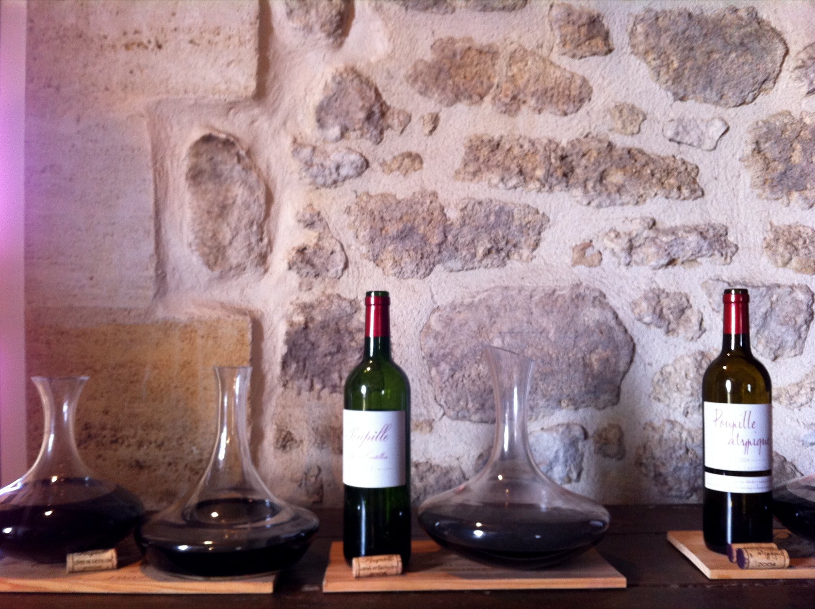 Des carafes de vin rouge et deux bouteilles de Château Poupille posées devant un mur de pierre