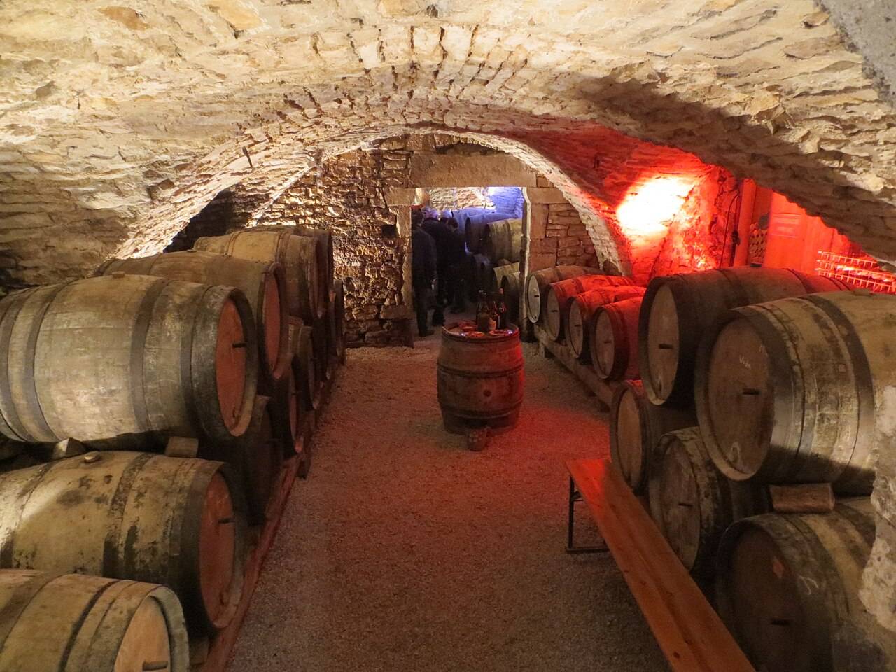 Des fûts de chêne alignés de part et d’autre d’une cave voûtée en pierre, à Château-Chalon