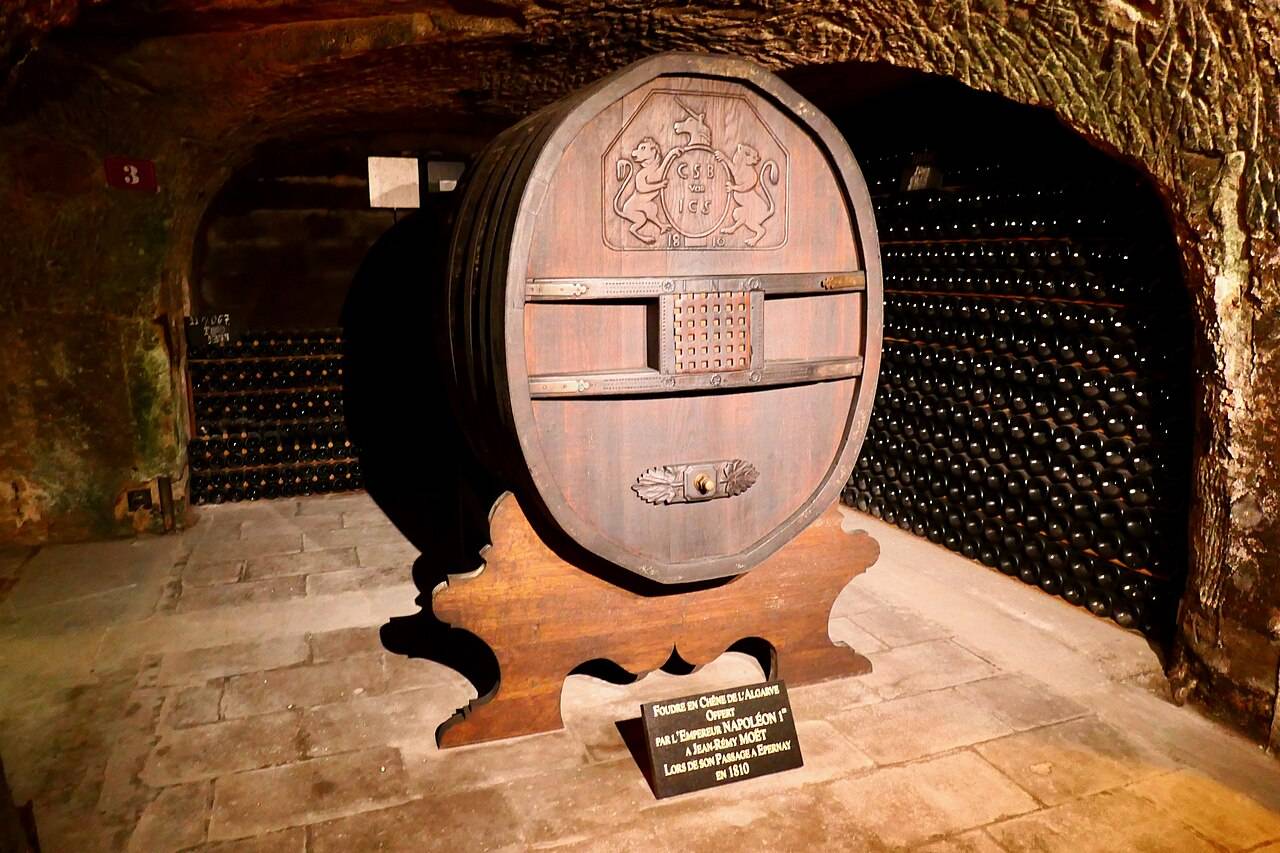 Un foudre de chêne sculpté dans une galerie de craie des caves Moët & Chandon, devant des piles de bouteilles