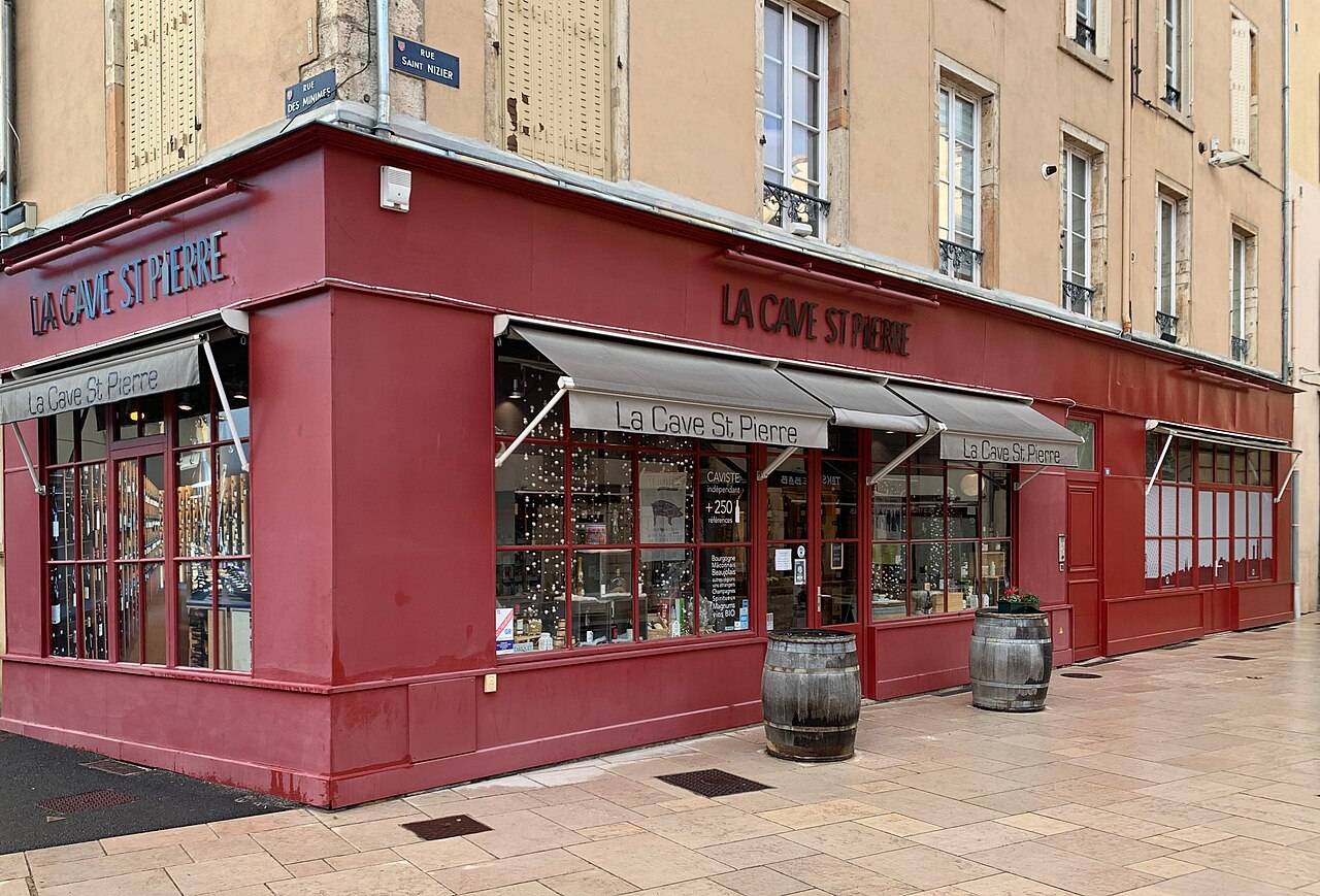 La devanture rouge de La Cave St Pierre, un caviste de Mâcon, à l’angle de deux rues, avec deux tonneaux sur le trottoir