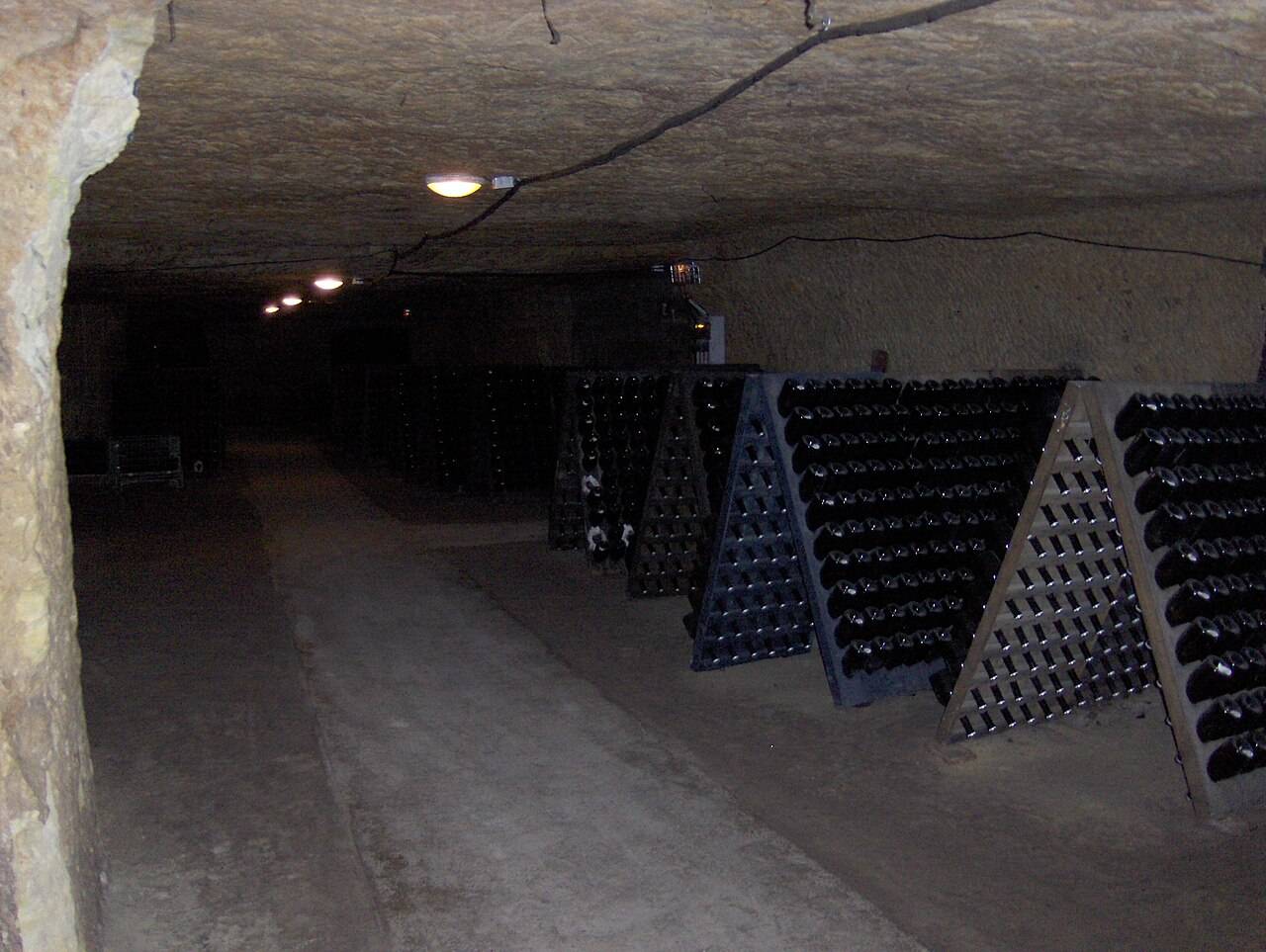 Une galerie creusée dans le tuffeau, à Vouvray, où des bouteilles reposent sur des pupitres