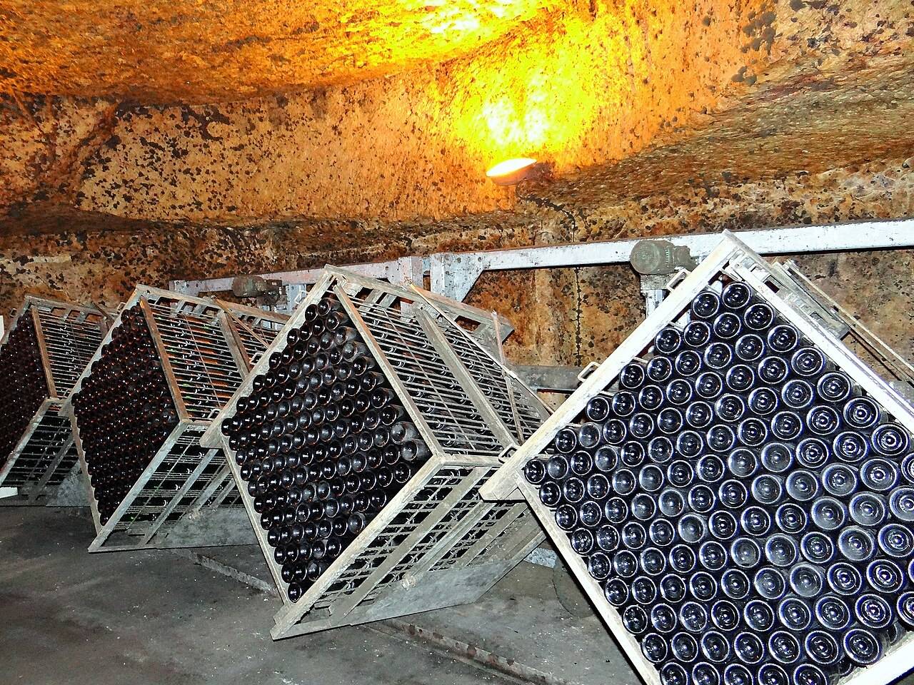 Des caisses métalliques pleines de bouteilles, inclinées pour le remuage, dans une ancienne carrière souterraine éclairée