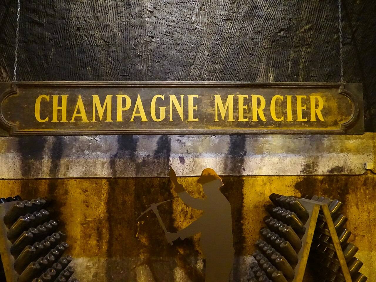 L’enseigne Champagne Mercier dans les caves, au-dessus de pupitres chargés de bouteilles et d’une silhouette de mineur creusant la craie