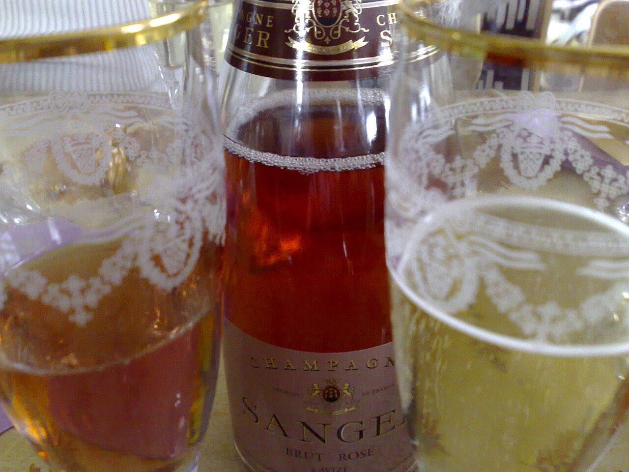 Un verre de champagne rosé et un verre de champagne blanc autour d’une bouteille de Sanger Brut Rosé