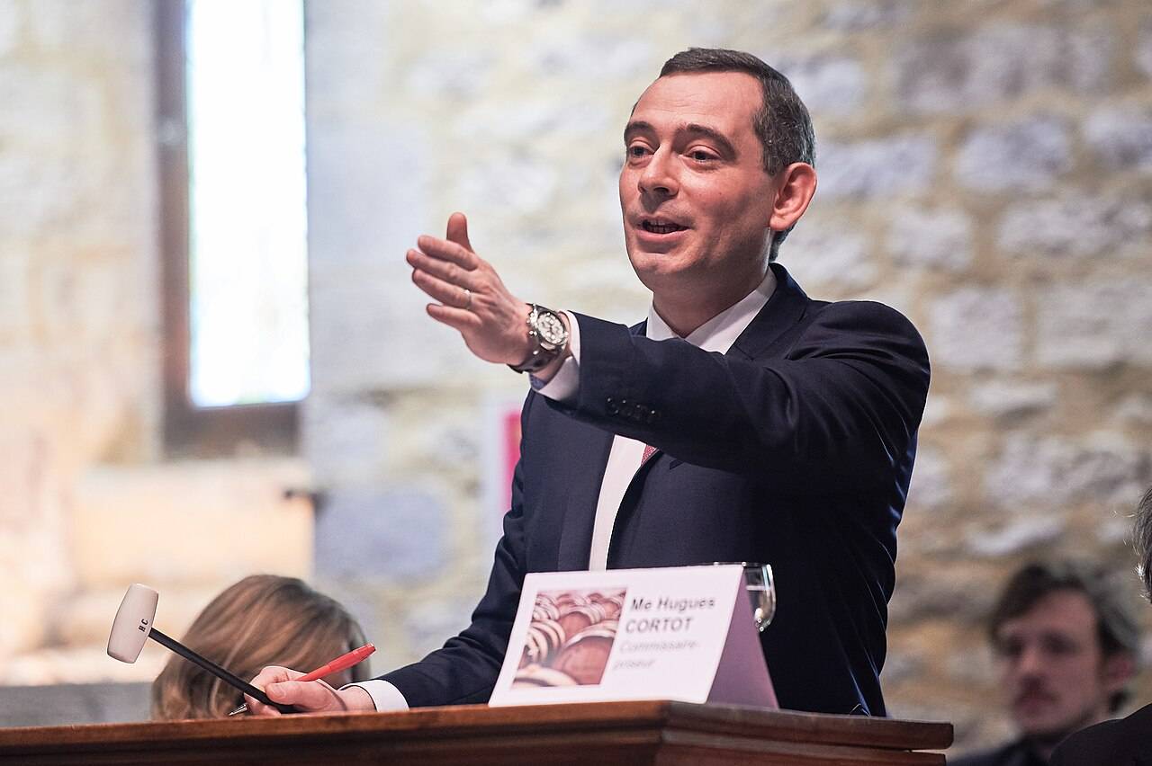 Un commissaire-priseur, bras tendu et marteau en main, à son pupitre pendant une vente aux enchères de vins