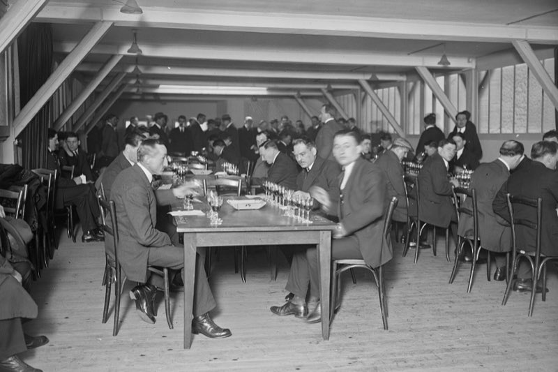 Des hommes en costume goûtent des vins autour de longues tables, lors d’un concours de dégustation à l’école des sommeliers, en 1926