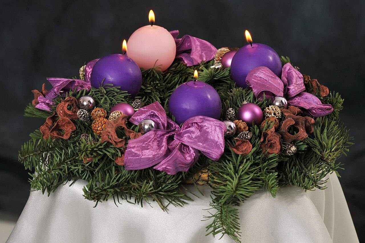 Une couronne de l’Avent en branches de sapin avec ses 4 bougies allumées, trois violettes et une rose
