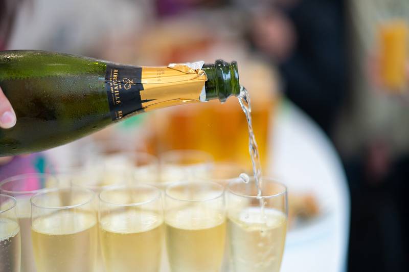 Une bouteille de crémant d’Alsace remplit une flûte, au-dessus d’un plateau de flûtes déjà servies