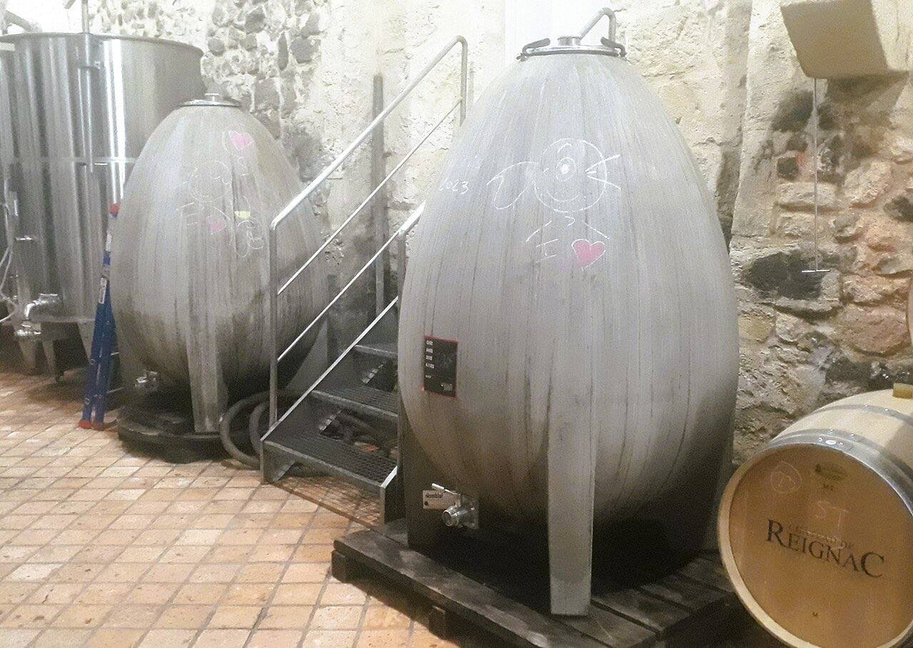 Deux cuves en béton en forme d’œuf dans un chai, à côté d’une barrique