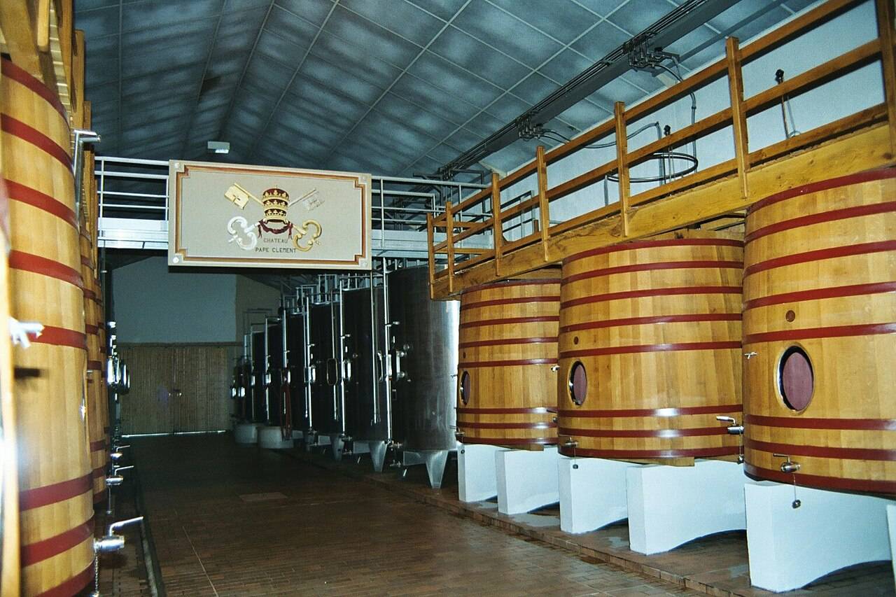 Le cuvier du Château Pape Clément, ses grandes cuves en bois cerclées de rouge et ses cuves en inox, sous les armoiries de la maison