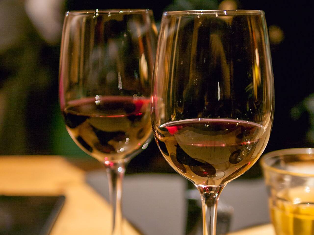 Deux verres à pied de vin rouge posés sur une table en bois, le soir