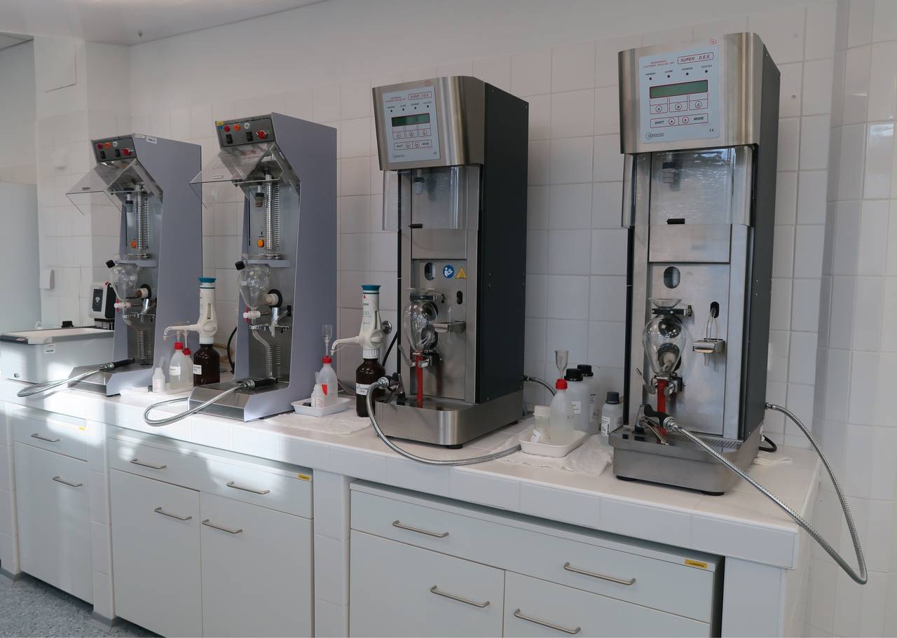 Quatre distillateurs de laboratoire alignés sur une paillasse carrelée de blanc, qui servent à mesurer le titre alcoométrique des vins