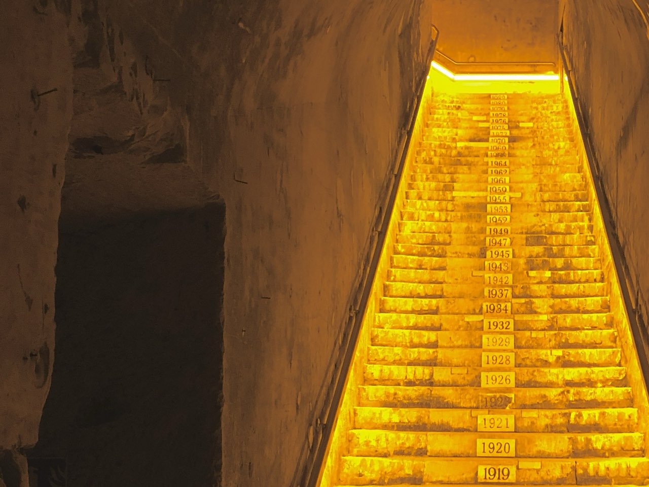 Un escalier de pierre éclairé dans une galerie de craie, chaque marche portant l’année d’un grand millésime