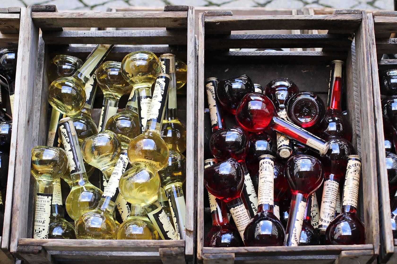 Deux caisses en bois remplies de petites bouteilles rondes de 0,2 litre, de vin blanc d’un côté et de vin rouge de l’autre
