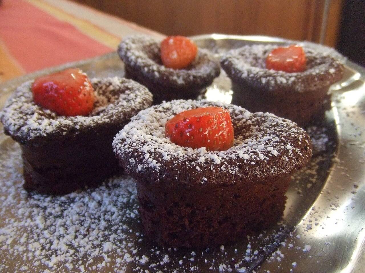 Des petits fondants au chocolat saupoudrés de sucre glace, chacun surmonté d’une fraise