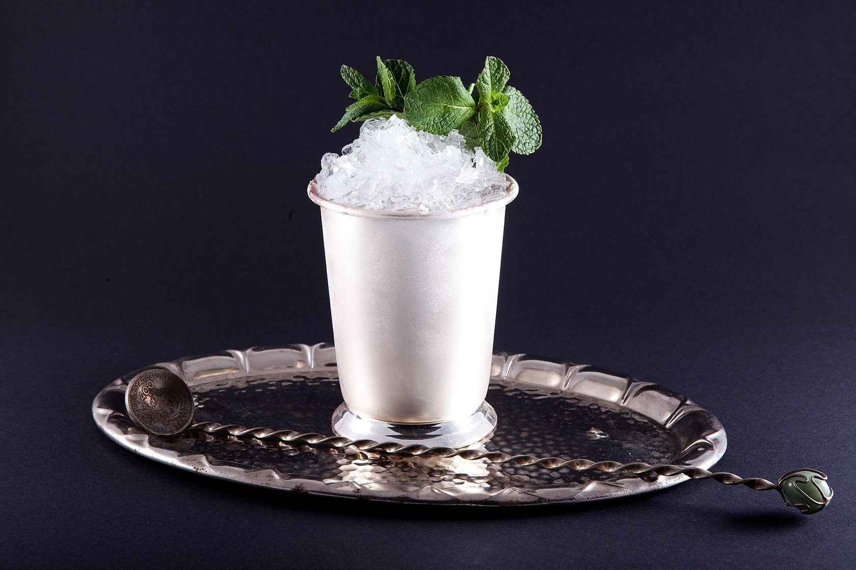 Un Mint Julep garni de menthe dans sa timbale en argent, posé sur un plateau avec une cuillère de bar