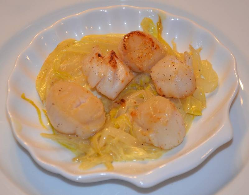Des noix de Saint-Jacques dorées posées sur une fondue de poireaux, dans une assiette blanche