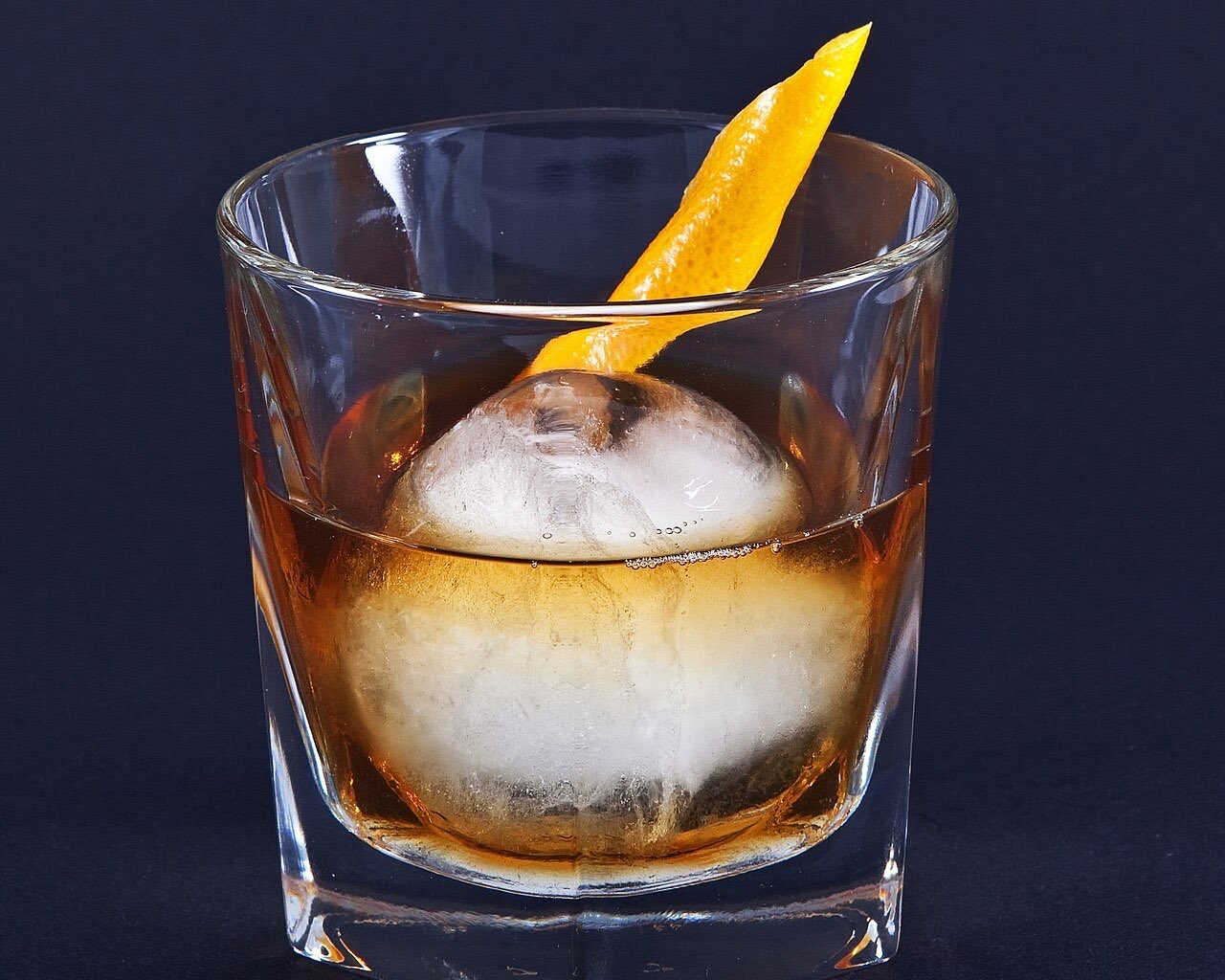 Un Old Fashioned sur une sphère de glace, avec un zeste d’orange, dans un verre bas