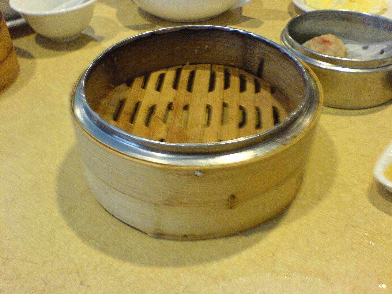 Un panier vapeur en bambou vide, à côté d’un petit panier contenant une bouchée, sur une table de restaurant