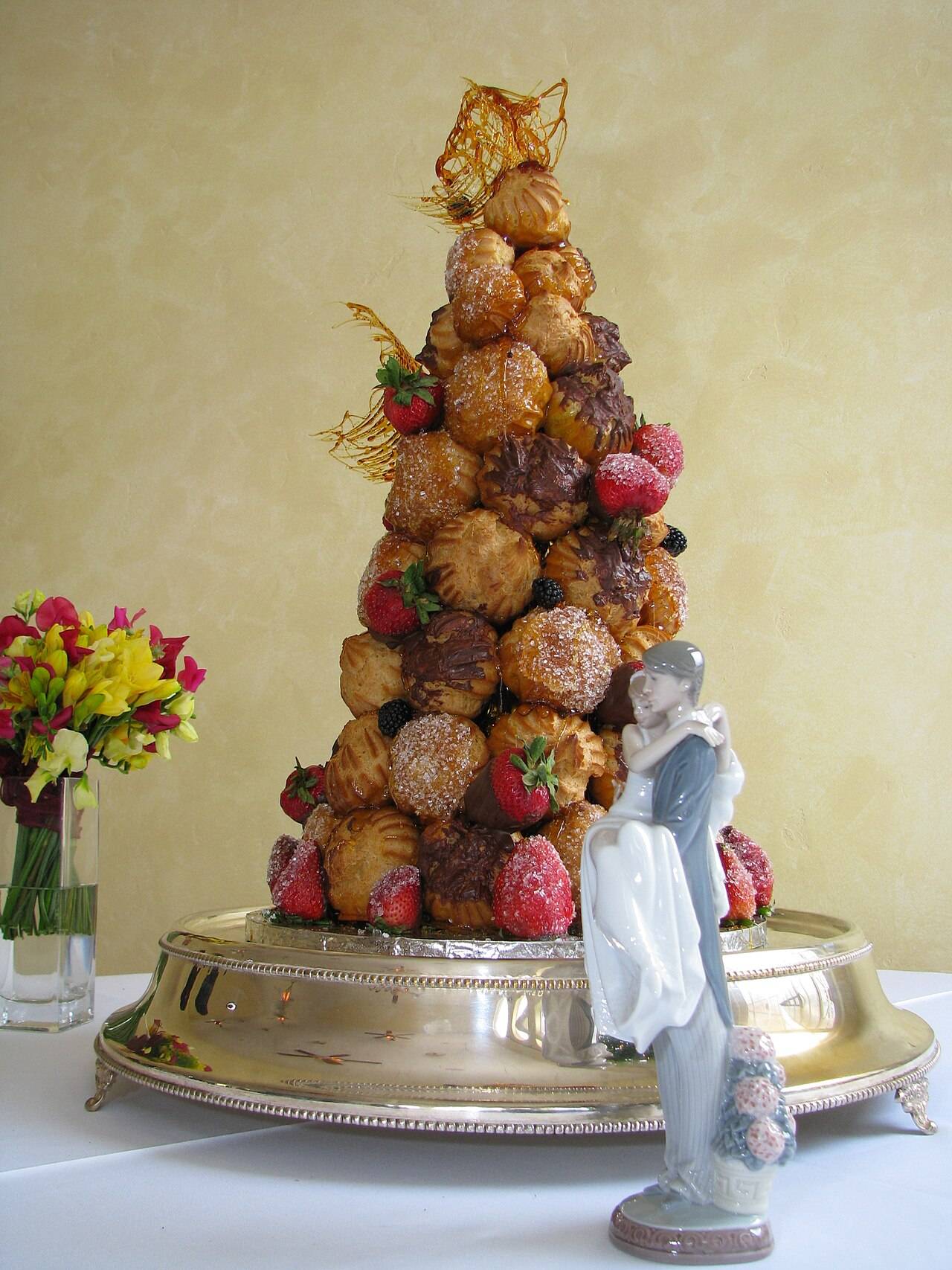 Une pièce montée de choux caramélisés et de fraises, avec une figurine de mariés et un bouquet de fleurs