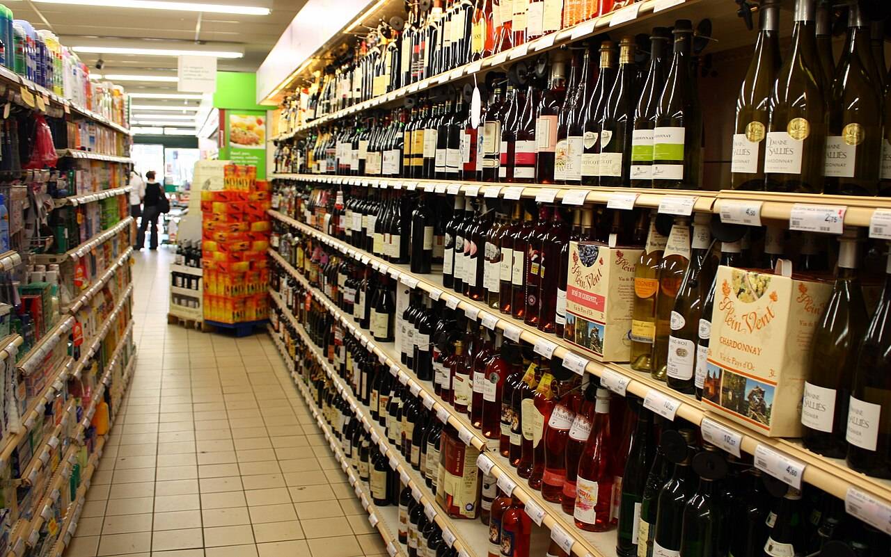 Le rayon des vins d’un supermarché, des bouteilles et des cubis alignés sur cinq étagères le long d’une allée