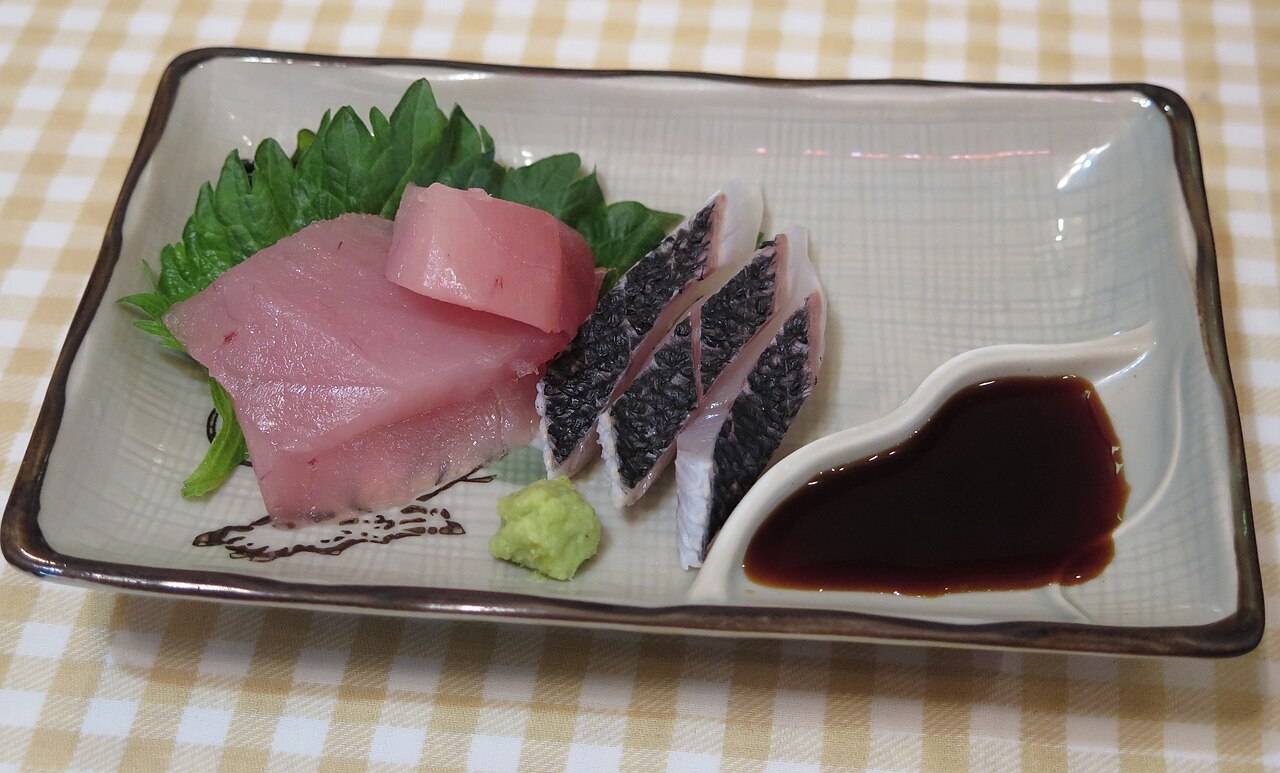 Des tranches de thon et de poisson blanc en sashimi, avec une feuille de shiso, du wasabi et de la sauce soja