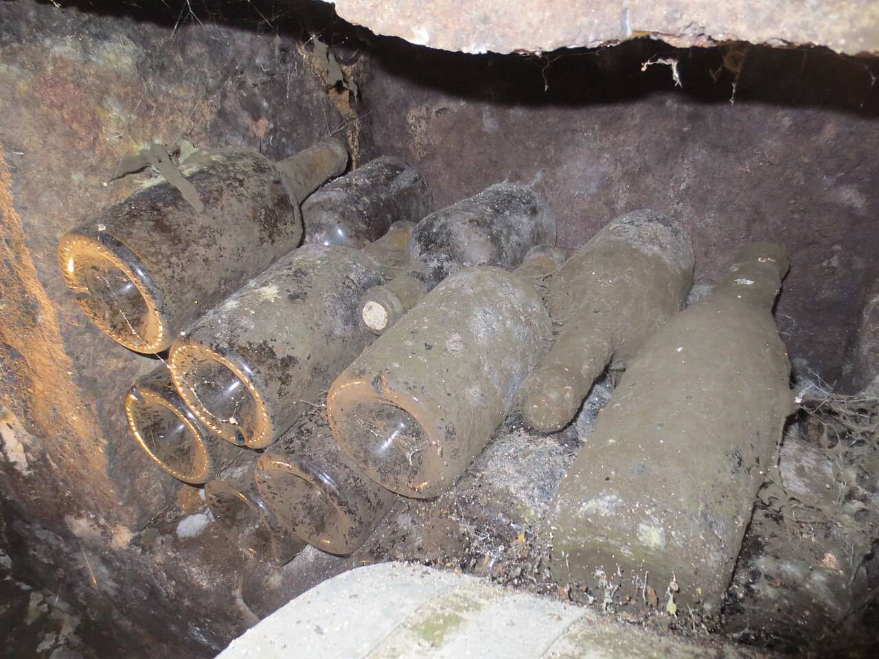 De vieilles bouteilles couvertes de poussière, de moisissure et de toiles d’araignée, couchées dans une niche de cave