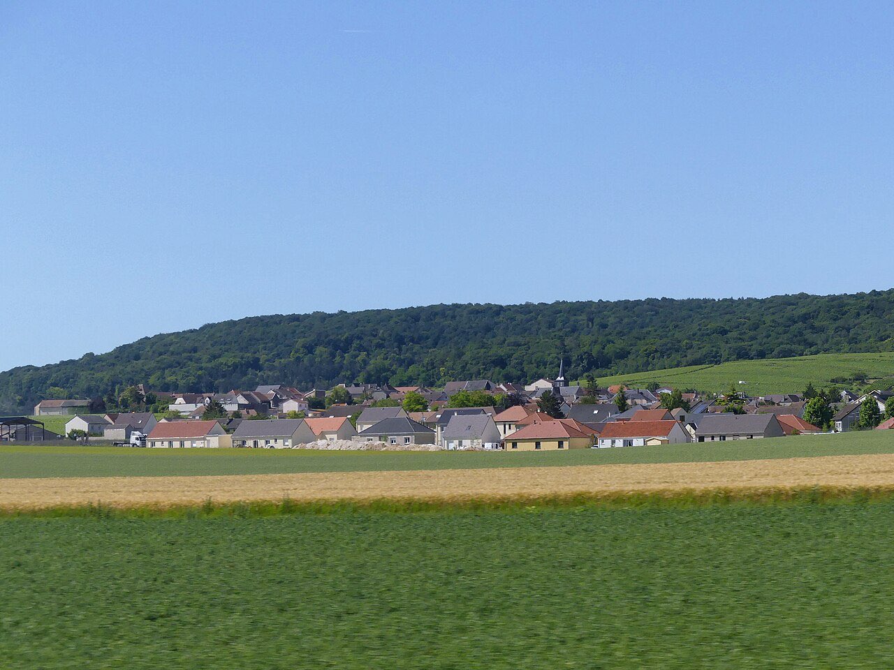 Le village de Villers-Marmery au pied de la Montagne de Reims, derrière un champ, vu depuis le train