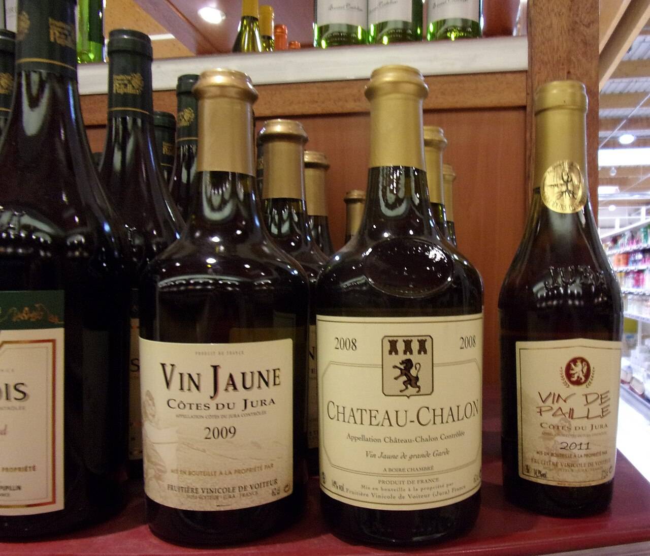Un vin jaune 2009 et un Château-Chalon 2008 en clavelin, à côté d’un vin de paille 2011 en demi-bouteille, sur l’étagère d’un magasin
